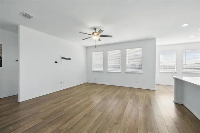 an empty room with wooden floor ceiling fan and windows