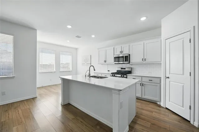 a kitchen with stainless steel appliances white cabinets a sink and wooden floor