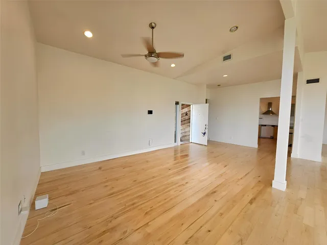 an empty room with wooden floor ceiling fan and kitchen view