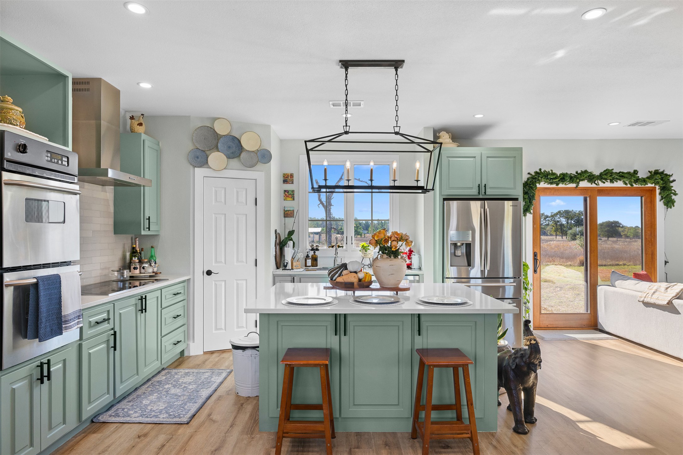 Kitchen featuring green cabinetry, appliances with stainless steel finishes, wall chimney range hood, a breakfast bar, and decorative light fixtures