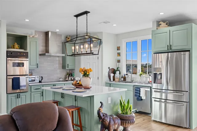 a kitchen with stainless steel appliances granite countertop a refrigerator a sink dishwasher a stove and a dining table with wooden floor