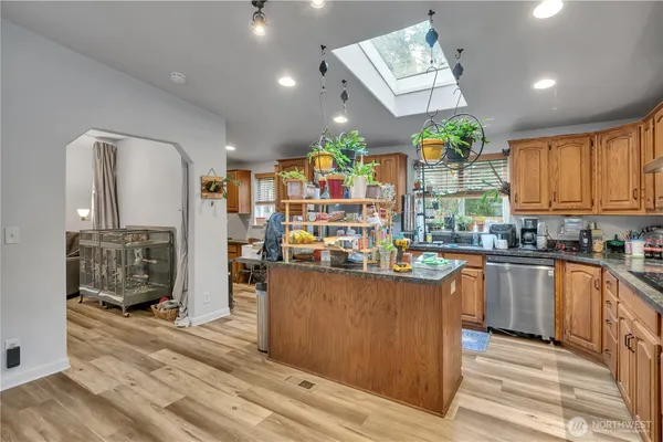 a kitchen with stainless steel appliances granite countertop a refrigerator a sink dishwasher a stove and a dining table with wooden floor