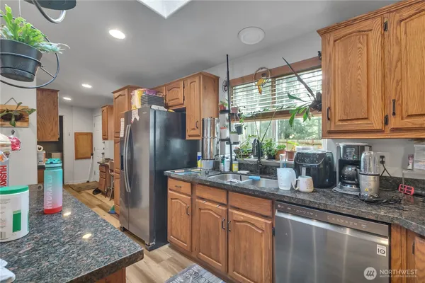 a kitchen with stainless steel appliances granite countertop a refrigerator a sink dishwasher and white cabinets with wooden floor