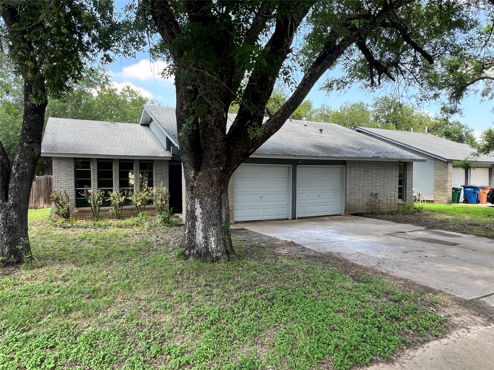 4620 Button Bend Road Austin, TX 78744 - Photo 1 of 22 Mature trees shade this charming brick residence, featuring an attached double garage and a neatly maintained lawn.