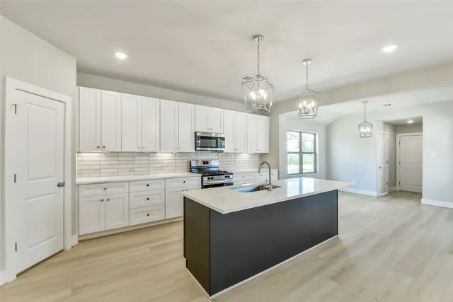 a large white kitchen with a large counter top space a sink stainless steel appliances and cabinets