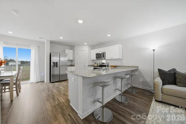 a kitchen with stainless steel appliances kitchen island granite countertop a refrigerator a sink a stove and white cabinets with wooden floor