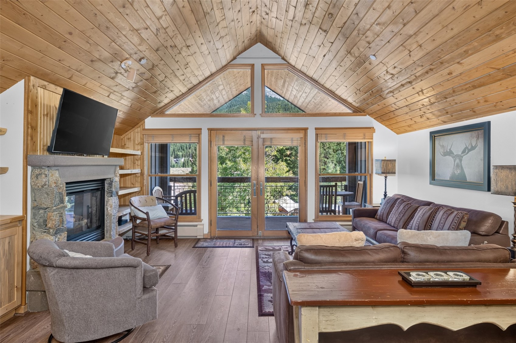 Vaulted wood-paneled ceiling, stone-clad fireplace, wood-finish flooring, built-in shelving, and transom windows