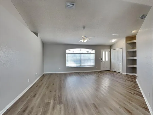an empty room with wooden floor chandelier and windows