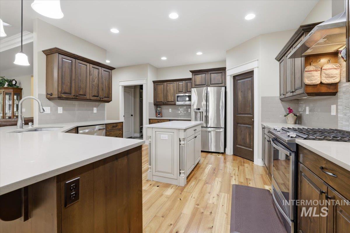 4604 Middlesboro Way Caldwell, ID 83607 - Photo 13 of 43 Kitchen with stainless steel appliances, dark brown cabinets, wall chimney exhaust hood, decorative light fixtures, and light wood-style floors