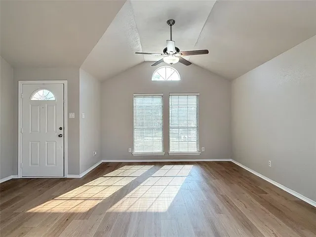 an empty room with wooden floor chandelier fan and windows