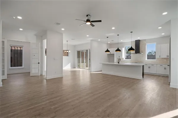 a view of an empty room and kitchen with hardwood floor