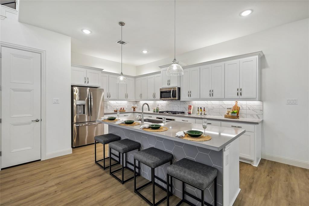 1604 Casting Ridge Mesquite, TX 75181 - Photo 14 of 38 Modern kitchen featuring white shaker cabinetry, stainless steel appliances, a light gray countertop island with hexagonal tile detailing, and wood-finish flooring