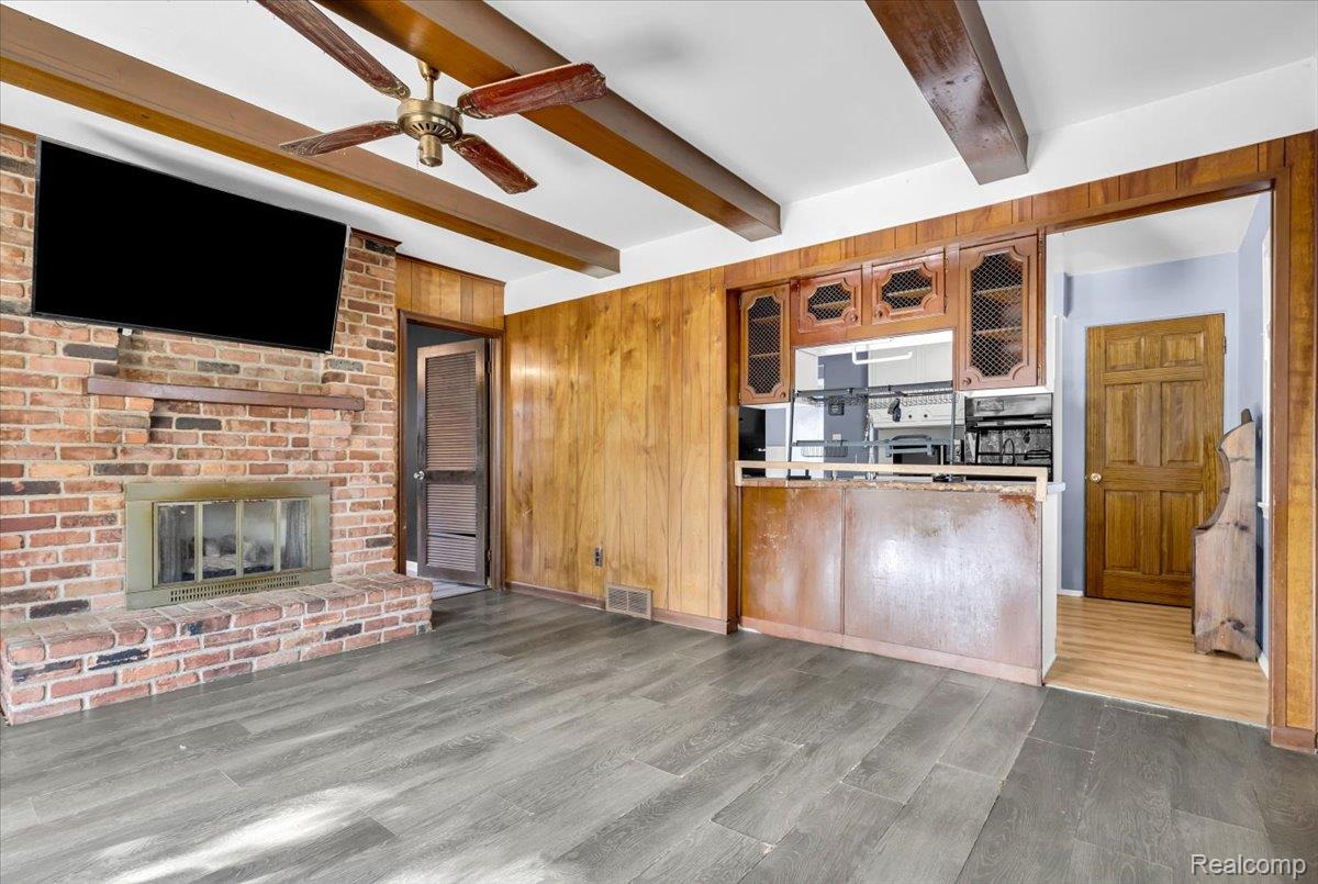 1215 Center Street Inkster, MI 48141 - Photo 6 of 30 Brick fireplace with a wood mantle, wood-finish flooring, wood paneling, wood ceiling beams, and a built-in kitchen pass-through with wood cabinetry