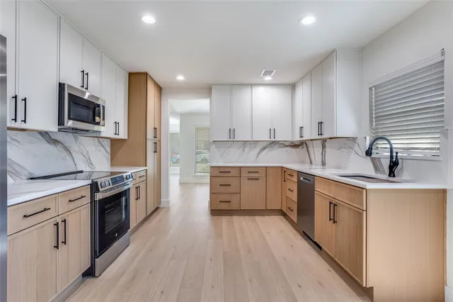 a kitchen with stainless steel appliances granite countertop a sink a stove top oven a refrigerator with white cabinets and wooden floor