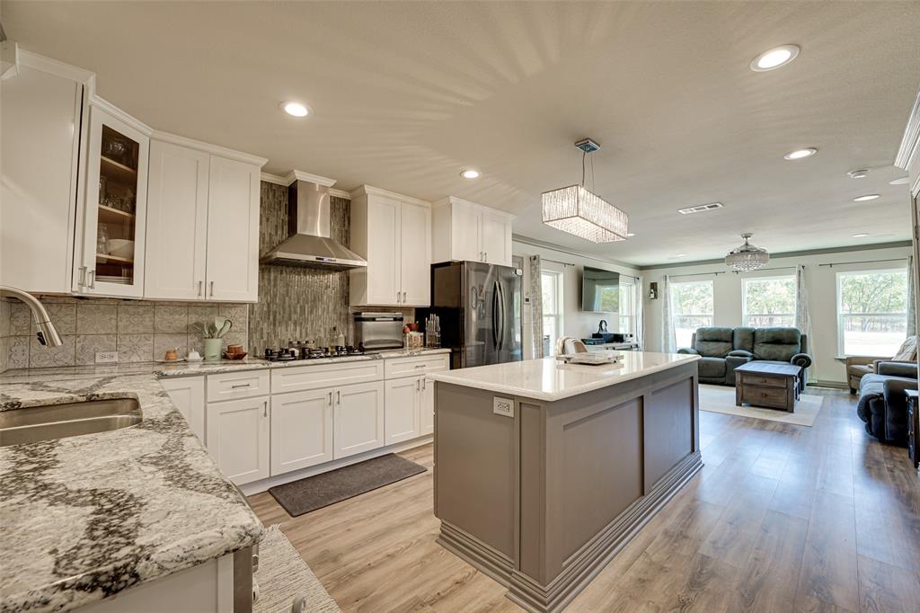 521 Bakers Branch Road Waxahachie, TX 75167 - Photo 15 of 37 Open-concept kitchen featuring white shaker cabinetry, granite countertops, a stainless steel range hood, an island with a white countertop, and wood-finish flooring