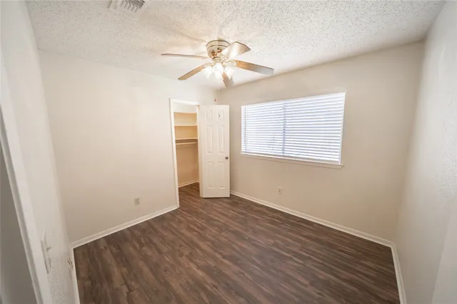 an empty room with wooden floor chandelier fan and windows