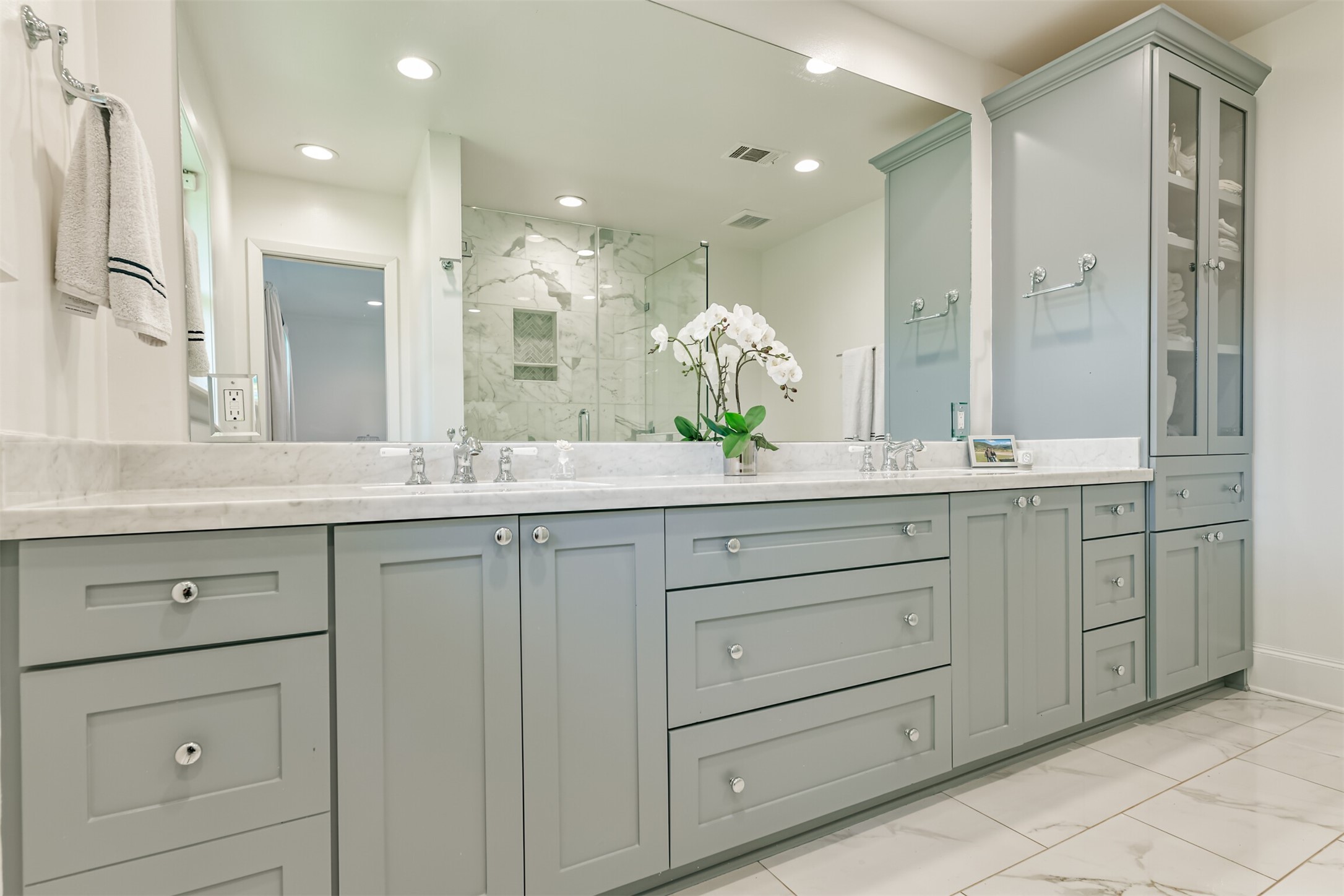 7819 Fairdale Lane Houston, TX 77063 - Photo 22 of 34 Dreamy primary bathroom, extensively updated in 2021. Features a spacious vanity with dual sinks, a large mirror, and a carrera marble countertop. Ample storage includes multiple drawers, cabinets, and a built-in glass-front linen display—designed for both elegance and function.