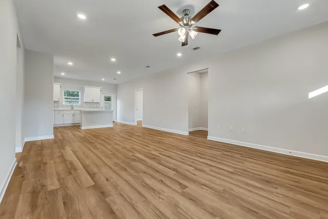 a view of an empty room with wooden floor and a ceiling fan