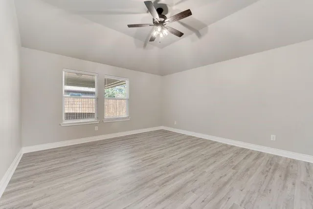 an empty room with wooden floor ceiling fan and windows