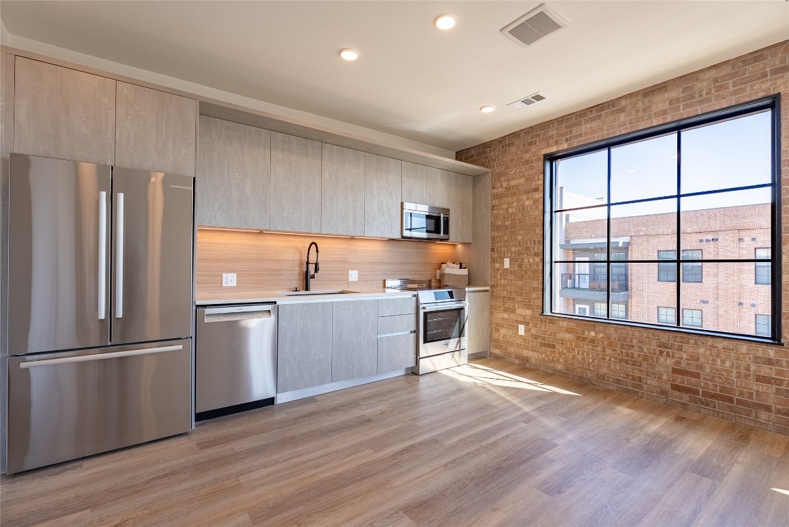 4315 South Congress Avenue, Unit 504 Austin, TX 78745 - Photo 3 of 21 Kitchen with brick wall, stainless steel appliances, modern cabinets, light wood-style floors, and recessed lighting