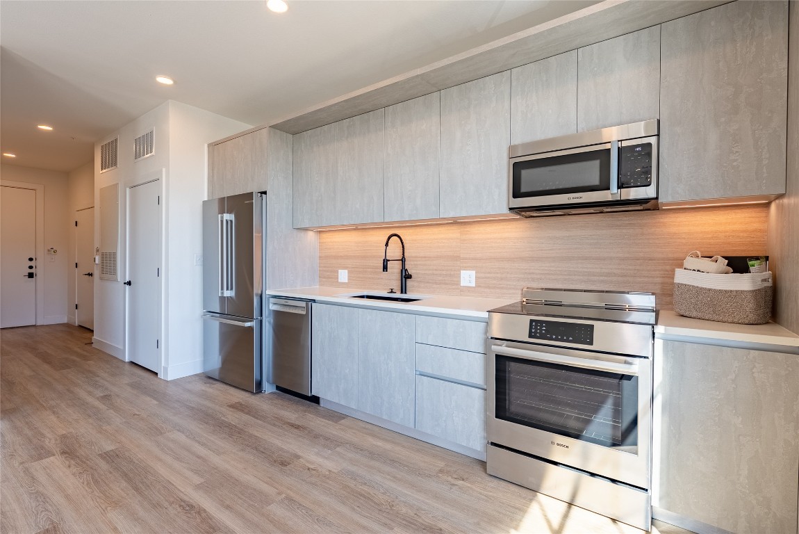 4315 South Congress Avenue, Unit 504 Austin, TX 78745 - Photo 4 of 21 Kitchen featuring modern cabinets, appliances with stainless steel finishes, light wood-type flooring, recessed lighting, and light stone counters
