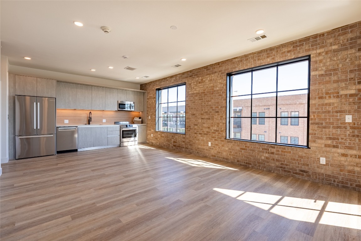 4315 South Congress Avenue, Unit 504 Austin, TX 78745 - Photo 5 of 21 Kitchen with appliances with stainless steel finishes, light countertops, brick wall, light wood-style floors, and modern cabinets