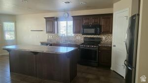 357 East 860 North Hurricane, UT 84737 - Photo 5 of 19 Kitchen featuring a central island with a light-toned countertop, wood-finish cabinetry, a patterned backsplash, and stainless steel appliances including a range and microwave
