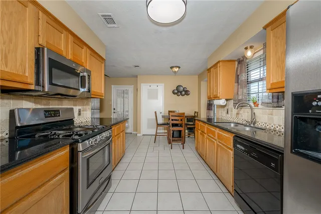 a kitchen with stainless steel appliances granite countertop a stove top oven a sink dishwasher a dining table and chairs with wooden floor