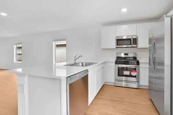 a kitchen with stainless steel appliances a stove top oven a sink a refrigerator and white cabinets