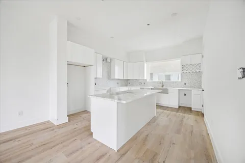 a large white kitchen with a sink dishwasher a refrigerator and white cabinets with wooden floor