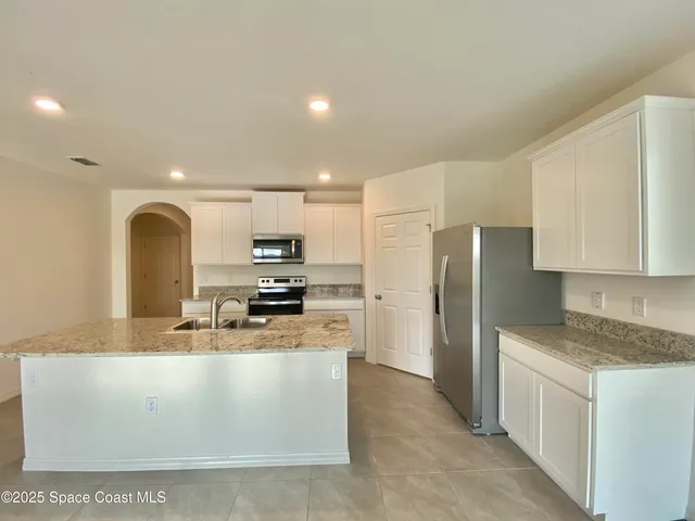 a large kitchen with stainless steel appliances granite countertop a stove a sink a refrigerator and white cabinets