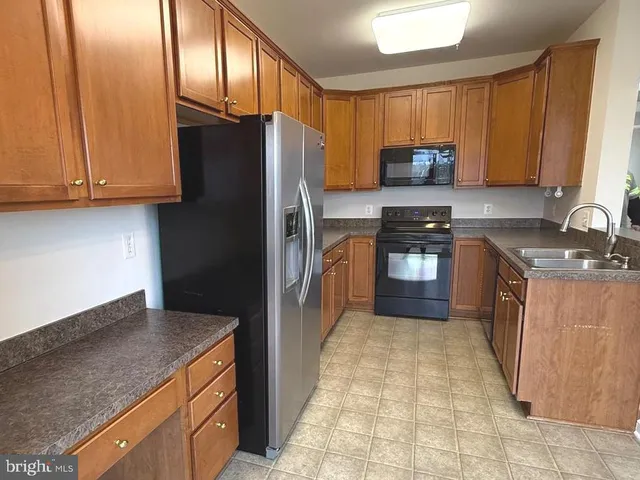 a kitchen with granite countertop a refrigerator a sink a stove top oven and cabinets
