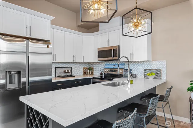 a kitchen with stainless steel appliances a stove refrigerator a sink dishwasher and white cabinets with wooden floor