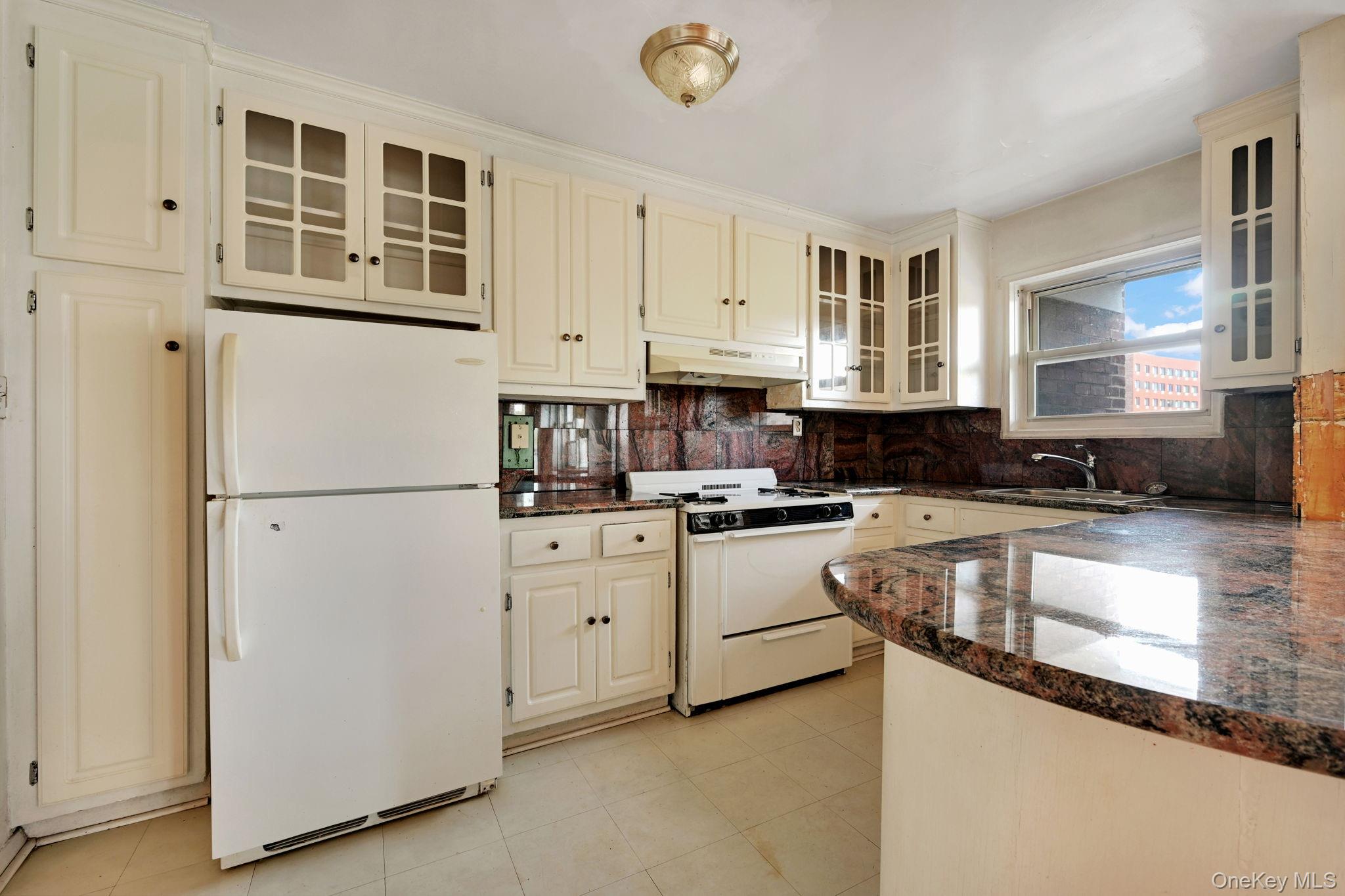 3131 Grand Concourse, Unit 3C Bronx, NY 10468 - Photo 21 of 27 a kitchen with granite countertop a refrigerator a stove a sink and white cabinets