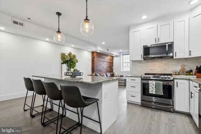 a kitchen with stainless steel appliances kitchen island granite countertop a stove top oven a sink a dining table and chairs with wooden floor