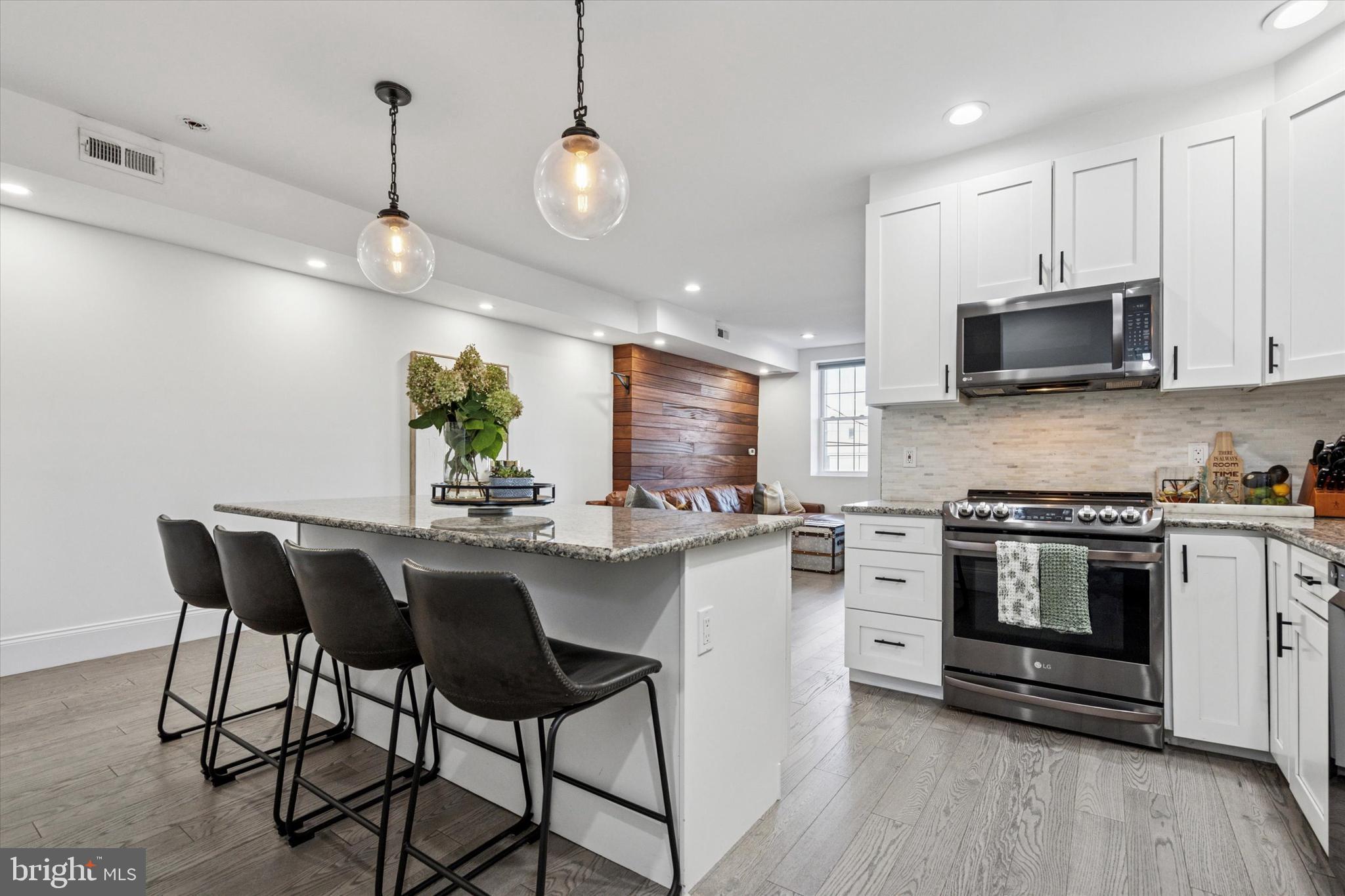 a kitchen with stainless steel appliances kitchen island granite countertop a stove top oven a sink a dining table and chairs with wooden floor