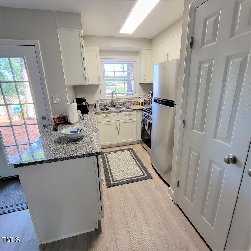 141 Jones Franklin Road, Unit E Raleigh, NC 27606 - Photo 4 of 20 a kitchen with granite countertop a refrigerator a sink dishwasher a stove and white cabinets with wooden floor