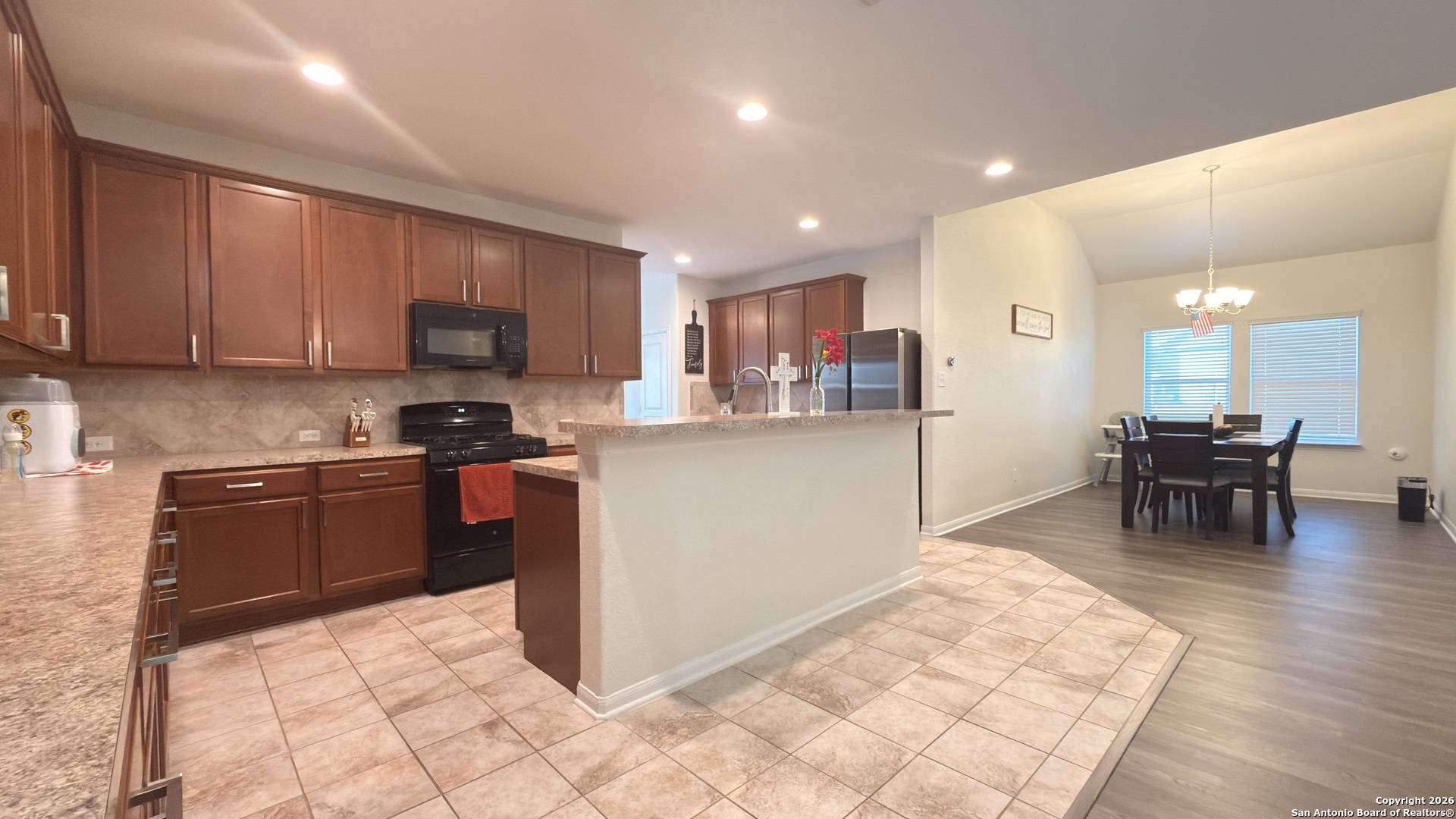 8949 Elizabeth Park Converse, TX 78109 - Photo 11 of 35 a kitchen with stainless steel appliances kitchen island granite countertop a stove a refrigerator a sink a dining table and chairs with wooden floor