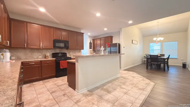 a kitchen with stainless steel appliances kitchen island granite countertop a stove a refrigerator a sink a dining table and chairs with wooden floor