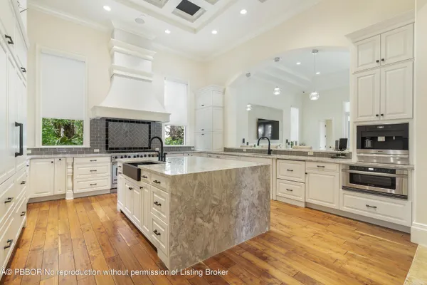 a large white kitchen with stainless steel appliances kitchen island granite countertop a large kitchen island a stove a sink a refrigerator and white cabinets with wooden floor