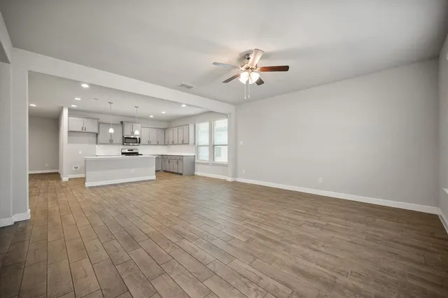 a view of an empty room with wooden floor and a kitchen