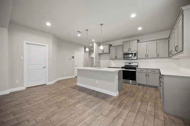 a large kitchen with kitchen island a sink dishwasher a stove and a refrigerator with wooden floor