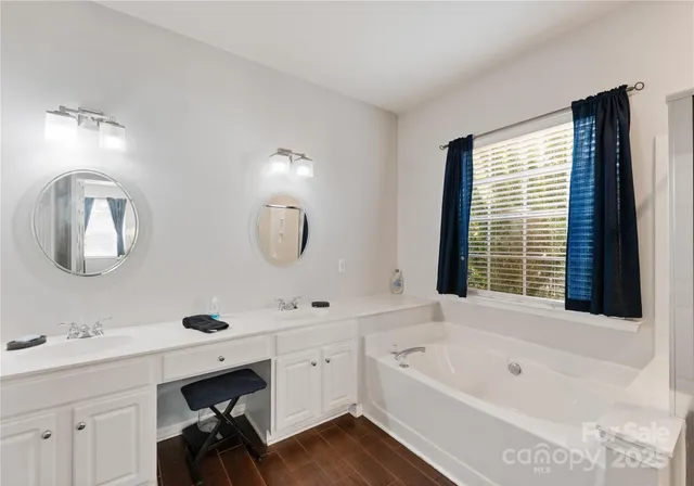 a bathroom with a tub double sink window and mirror