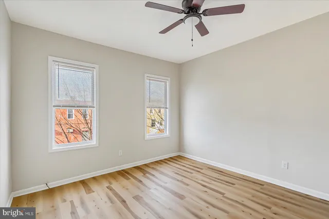 an empty room with wooden floor fan and windows