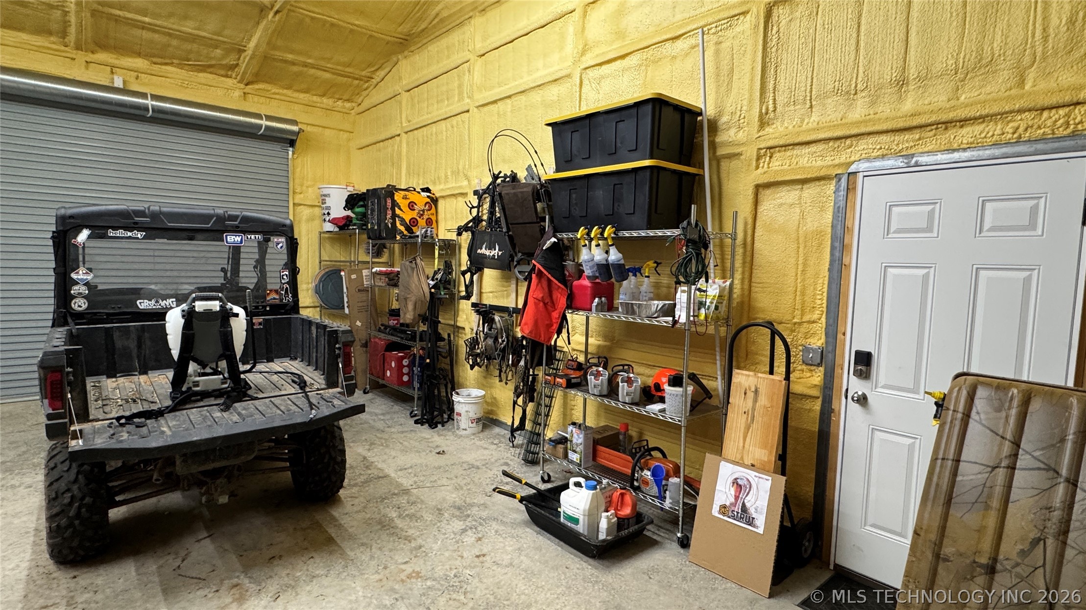 20862 East 1160th Road Keota, OK 74941 - Photo 40 of 47 Garage space featuring a roll-up door, paneled entry door, concrete flooring, and spray foam insulation on walls and ceiling