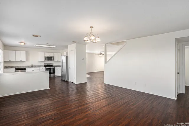 a view of an empty room and kitchen with wooden floor