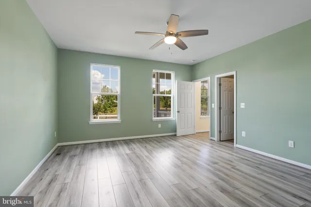 an empty room with wooden floor chandelier fan and windows