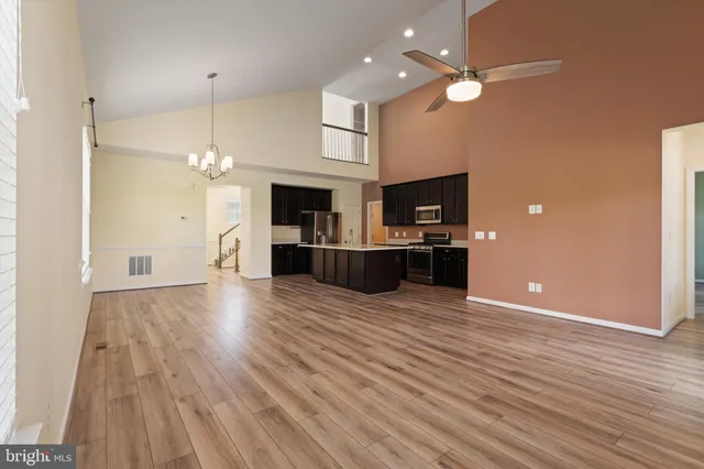 an empty room with wooden floor a fireplace a kitchen view and a chandelier