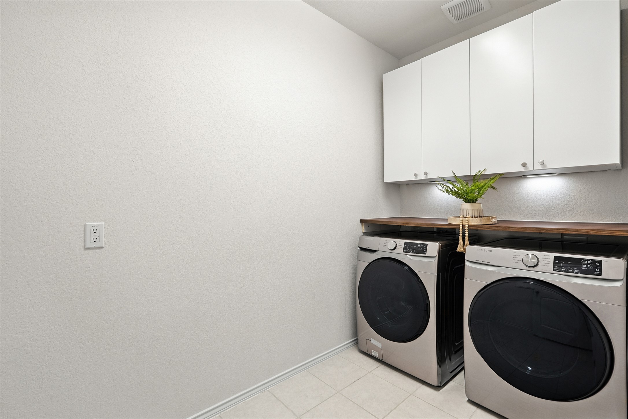 211 Brookside Street Hutto, TX 78634 - Photo 21 of 40 Laundry area featuring washing machine and dryer, light tile patterned flooring, cabinet space, and a textured wall