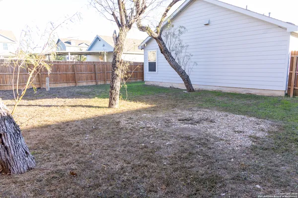 a view of a backyard with large trees and wooden fence